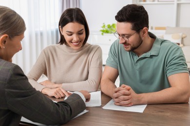 Young couple consulting insurance agent about pension plan at wooden table indoors