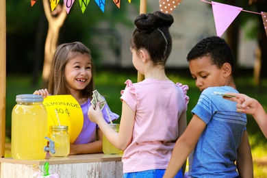 Little girl selling natural lemonade to kids in park. Summer refreshing drink