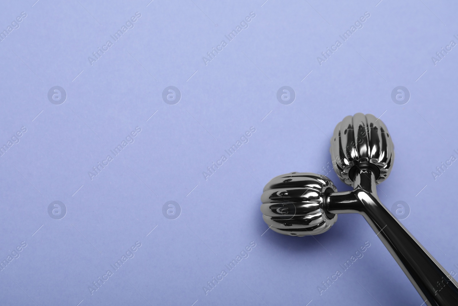 Photo of Metal face roller on lilac background, top view. Space for text