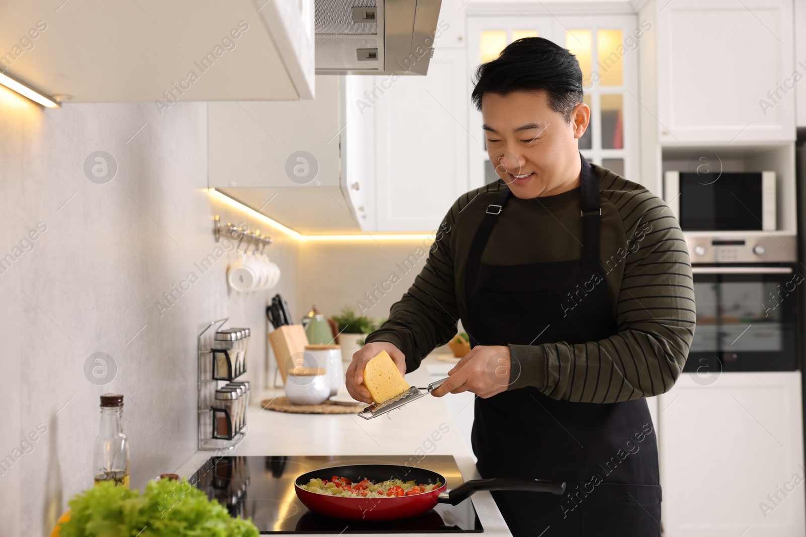 Photo of Cooking process. Man grating cheese into frying pan in kitchen