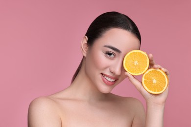 Beautiful young woman with pieces of orange on pink background