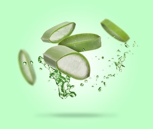 Sliced aloe vera leaf and splashes of juice on green background