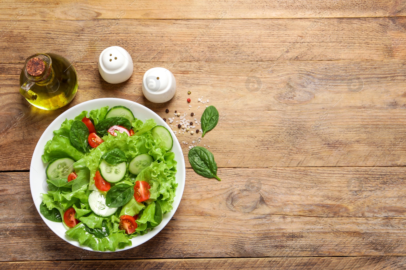 Photo of Delicious salad, oil, salt and pepper shakers on wooden table, flat lay. Space for text