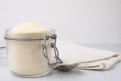 Photo of Uncooked organic semolina in jar and spoon on white tiled table, closeup. Space for text