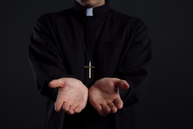 Priest reaching out his hands on black background, closeup