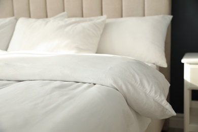 Comfortable bed with soft blanket and pillows indoors, closeup