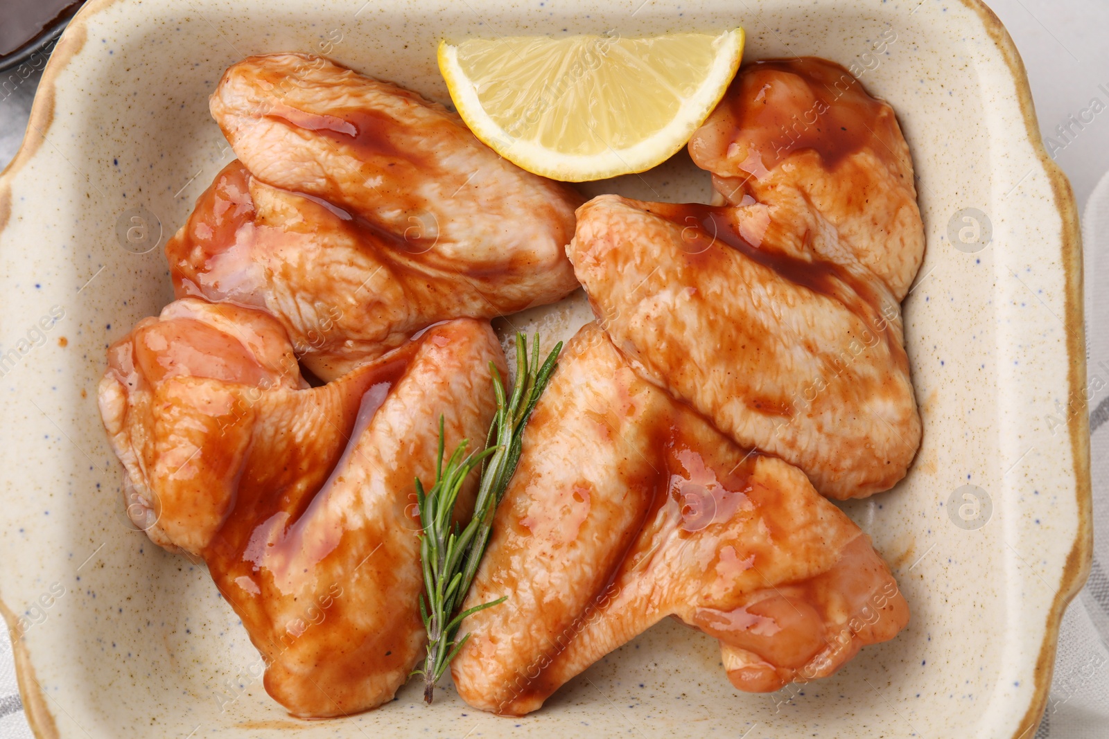 Photo of Raw marinated chicken wings, rosemary and lemon in baking dish on table, top view