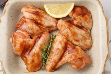 Raw marinated chicken wings, rosemary and lemon in baking dish on table, top view