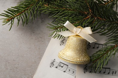 Golden shiny bell with bow, music sheets and fir branches on light table, flat lay. Space for text. Christmas decoration