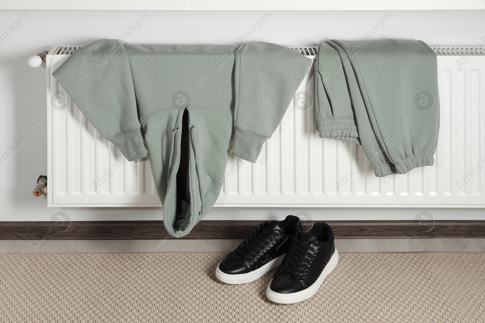 Photo of Heating radiator with clothes and shoes in room