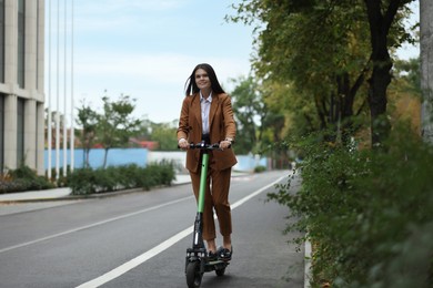 Photo of Young businesswoman riding electric kick scooter outdoors