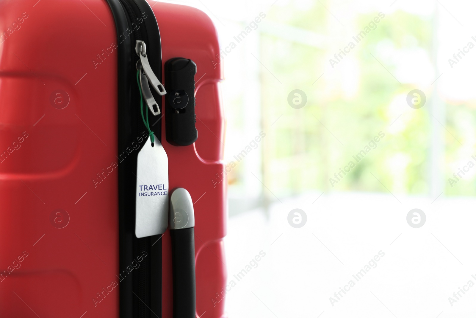 Photo of Stylish suitcase with travel insurance label on blurred background, closeup. Space for text