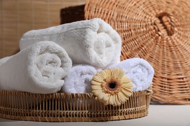 Photo of Rolled terry towels and flower on white table indoors