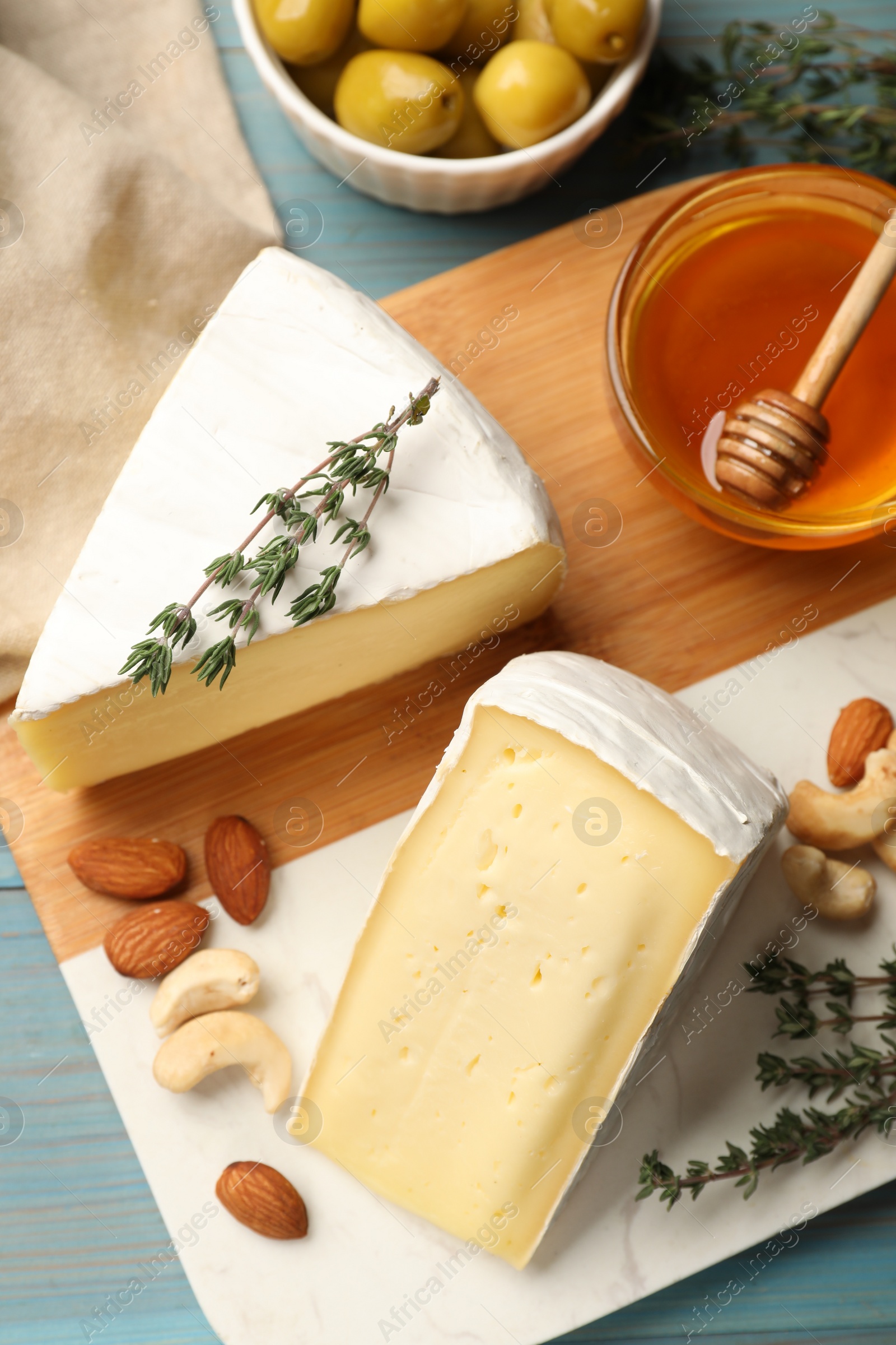 Photo of Tasty Camembert cheese with thyme, honey and nuts on light blue wooden table, flat lay