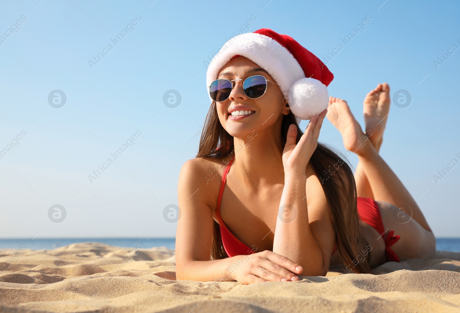 Photo of Beautiful young woman in Santa hat and bikini on beach, space for text. Christmas vacation