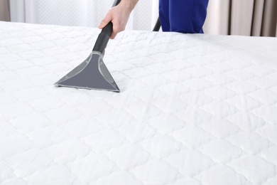 Man disinfecting mattress with vacuum cleaner, closeup. Space for text