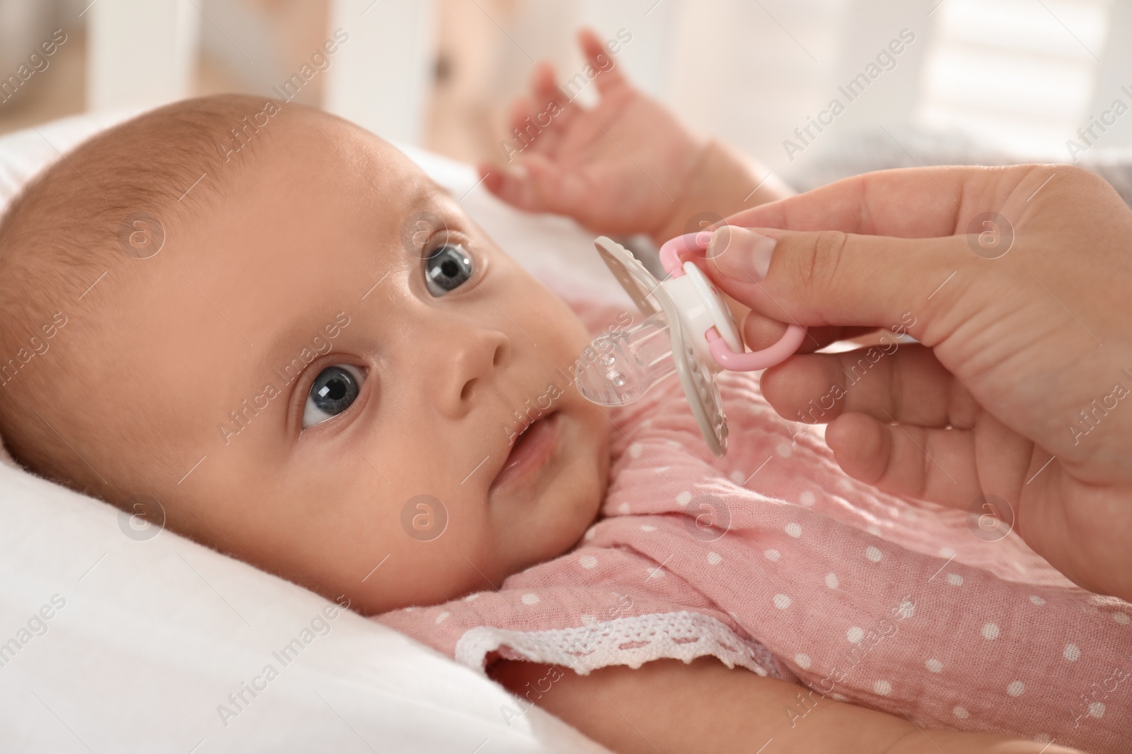 Photo of Mother giving pacifier to cute little baby in soft crib, closeup