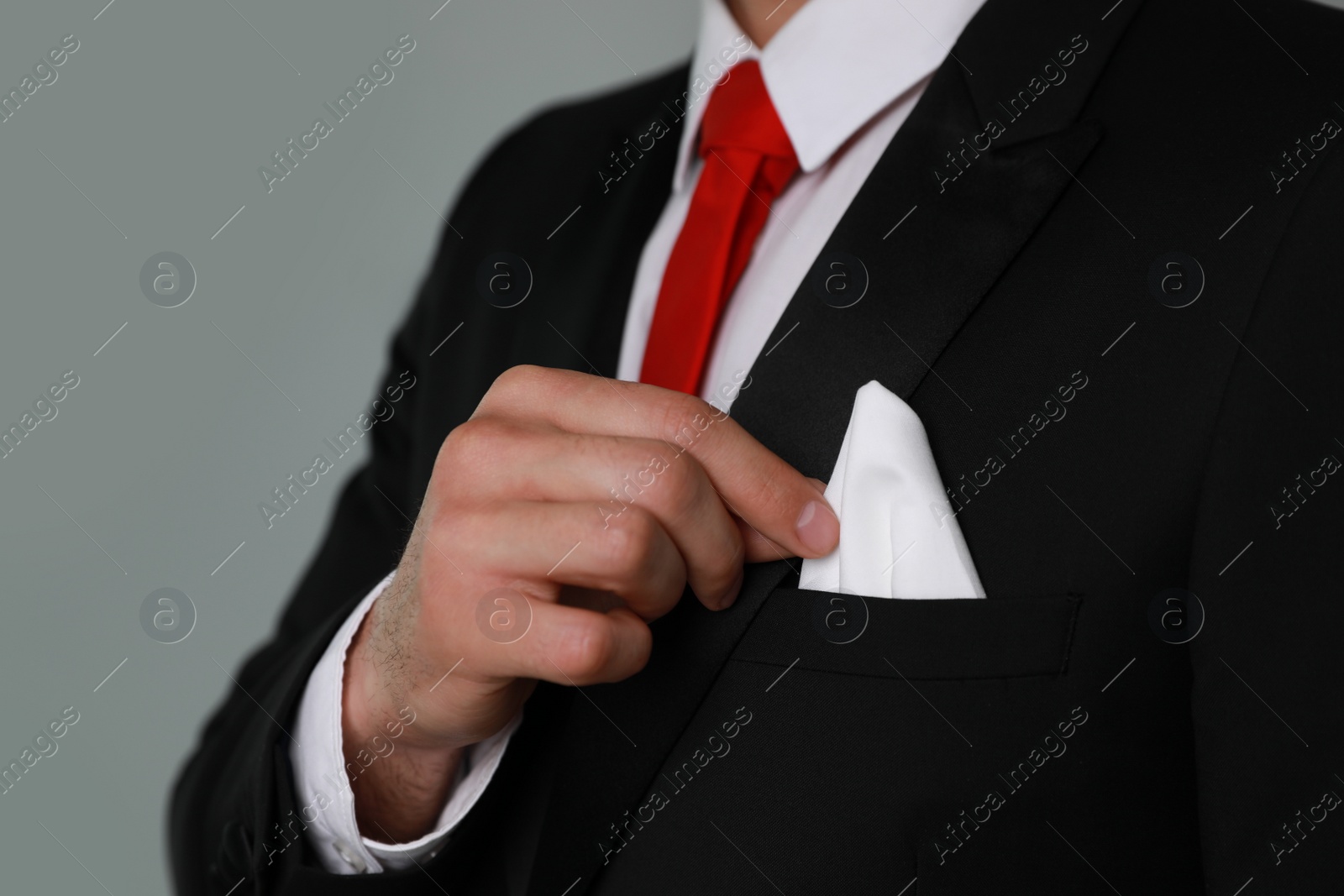 Photo of Man taking handkerchief from suit pocket on grey background, closeup