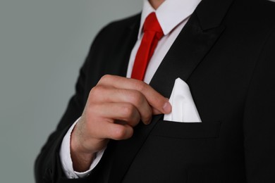 Photo of Man taking handkerchief from suit pocket on grey background, closeup