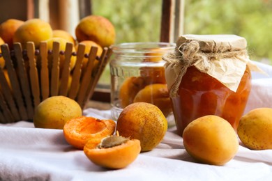 Jar of delicious jam and fresh ripe apricots on tablecloth indoors. Fruit preserve