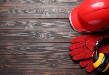 Photo of Hard hat, protective gloves and earmuffs on wooden background, flat lay. Space for text