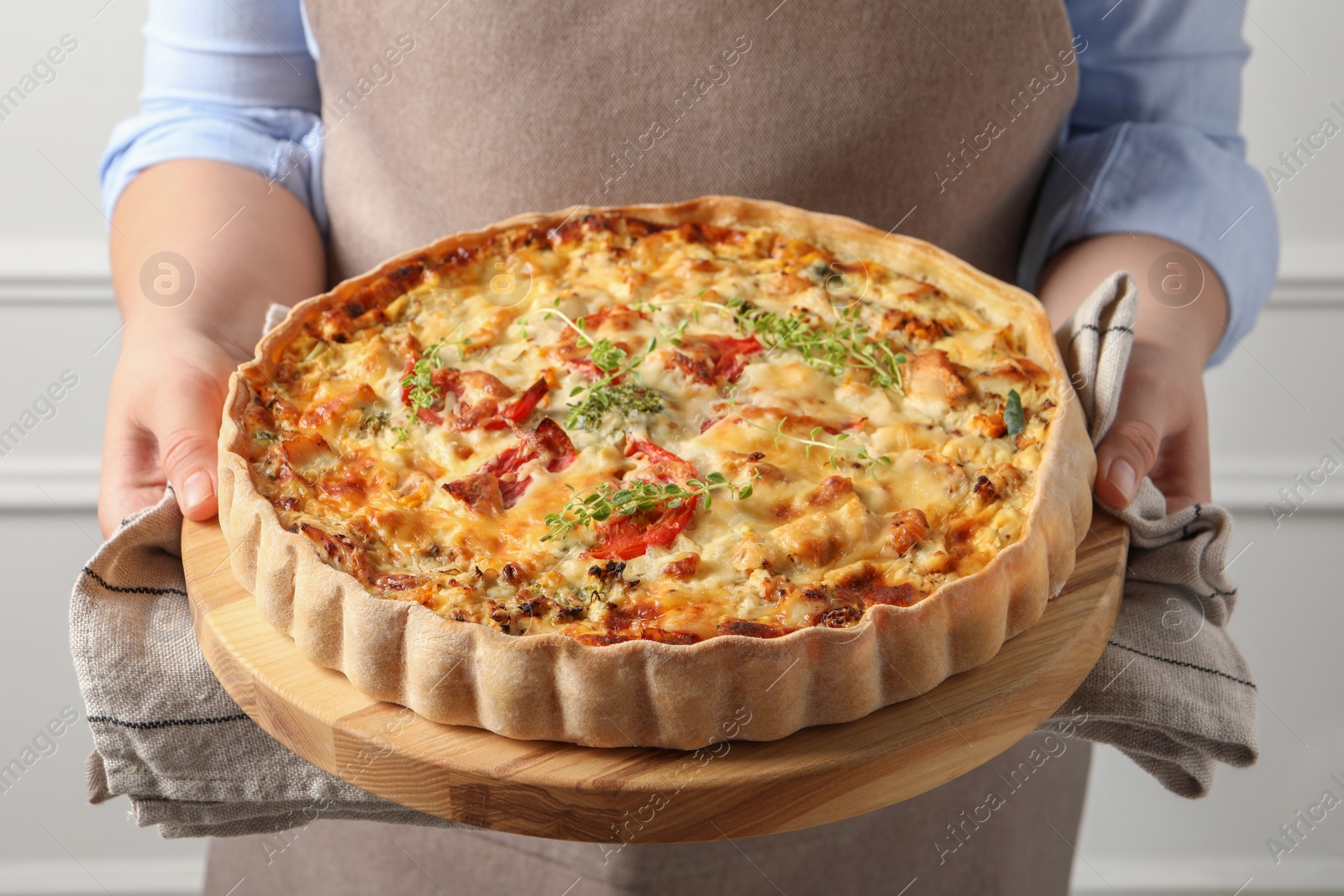 Photo of Woman holding board with tasty quiche indoors, closeup