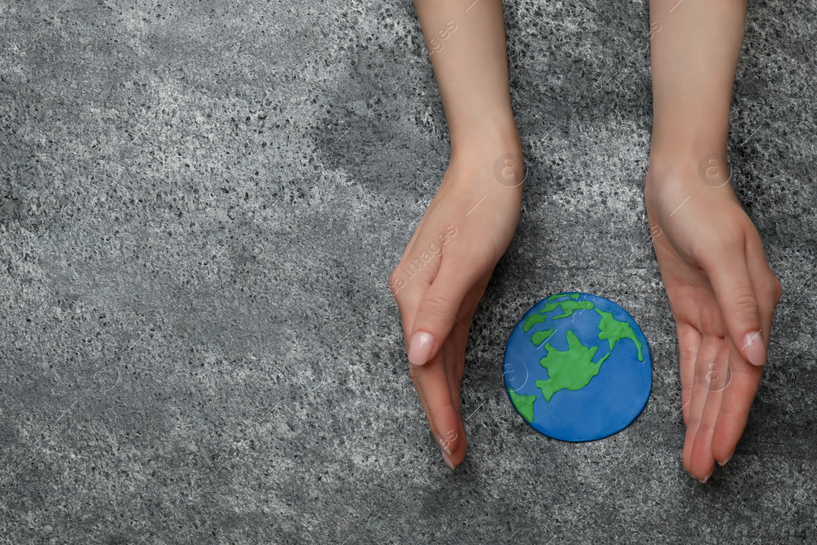 Photo of Happy Earth Day. Woman with plasticine planet at grey table, top view and space for text