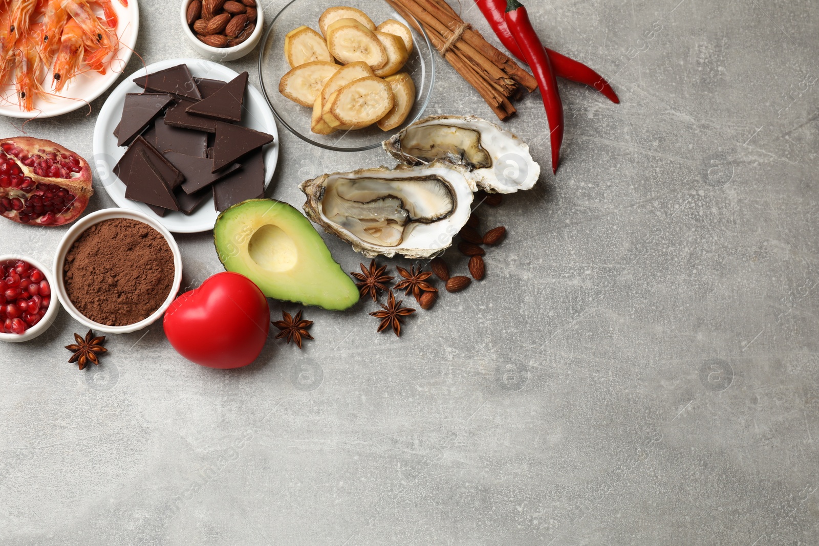 Photo of Natural aphrodisiac. Different food products and heart model on grey table, flat lay. Space for text