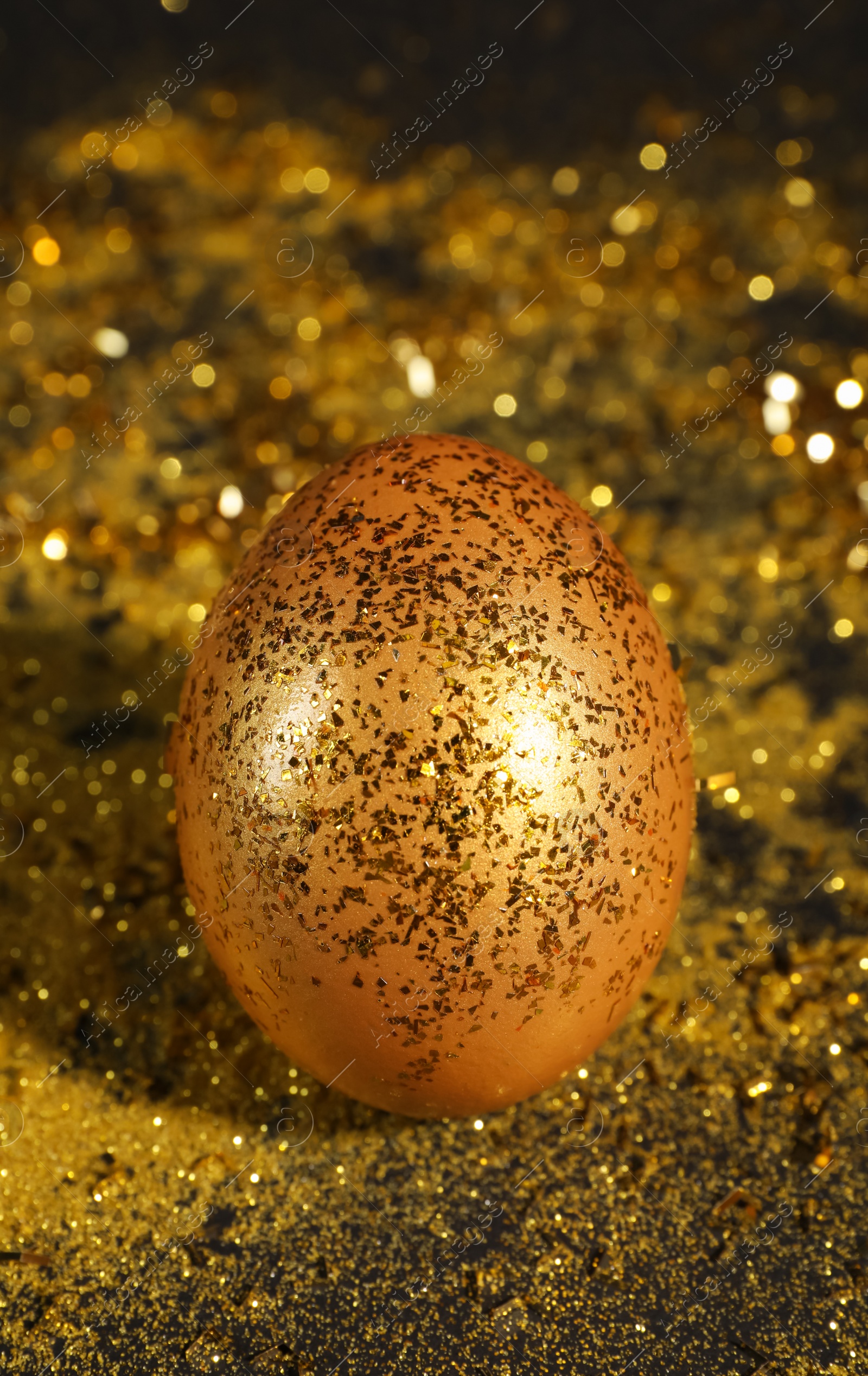 Photo of Shiny golden egg with glitter on dark table