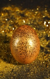 Photo of Shiny golden egg with glitter on dark table