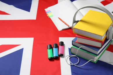 Photo of Learning foreign language. Different books, headphones and stationery on flag of United Kingdom, space for text