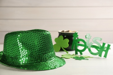 Photo of Green sequin hat, decorative clover leaves and party glasses on white wooden table. St Patrick's Day celebration