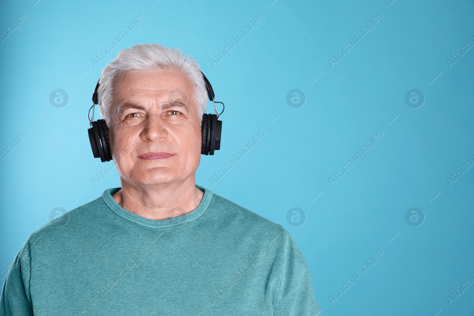 Photo of Mature man enjoying music in headphones on color background. Space for text