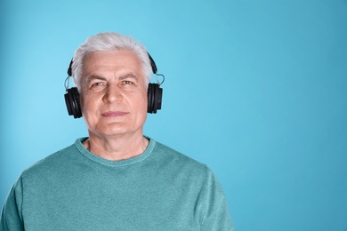 Mature man enjoying music in headphones on color background. Space for text