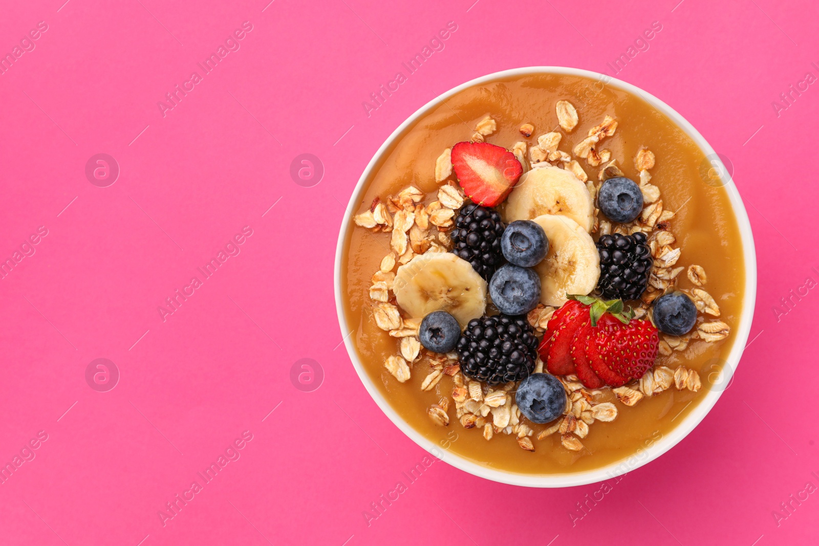Photo of Delicious smoothie bowl with fresh berries, banana and oatmeal on pink background, top view. Space for text