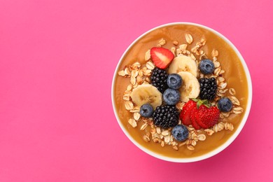 Photo of Delicious smoothie bowl with fresh berries, banana and oatmeal on pink background, top view. Space for text