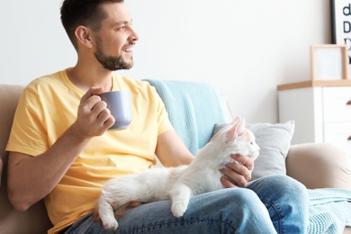 Photo of Young man with cute cat on sofa at home