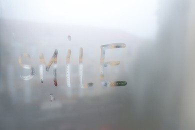 Photo of Word SMILE written on foggy window. Rainy weather