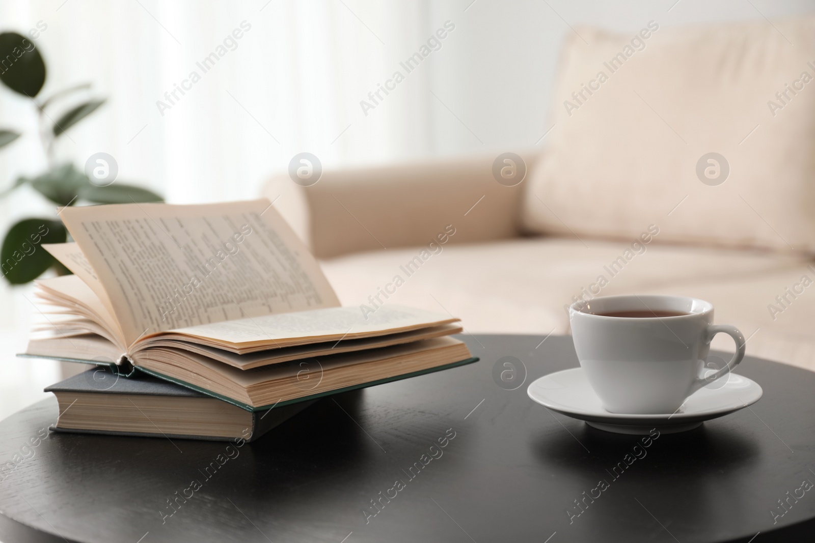 Photo of Books and cup of tea on table near modern sofa indoors. Home interior