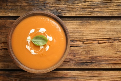 Photo of Tasty creamy pumpkin soup with basil in bowl on wooden table, top view. Space for text