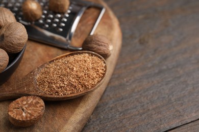 Photo of Spoon with grated nutmeg, seeds and grater on wooden table, closeup. Space for text