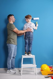 Photo of Father and son painting wall with roller indoors, back view. Repair work