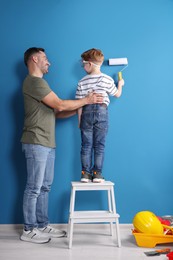 Father and son painting wall with roller indoors, back view. Repair work