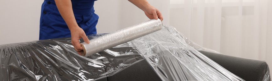 Image of Worker wrapping sofa in stretch film indoors, closeup. Banner design