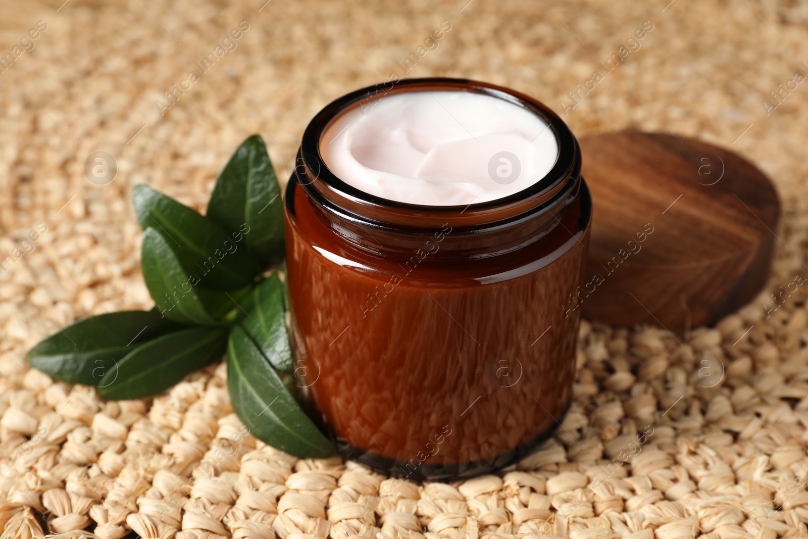 Photo of Jar of face cream and green leaves on wicker mat