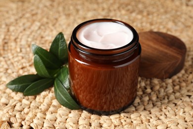 Jar of face cream and green leaves on wicker mat