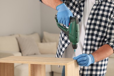 Photo of Man with electric screwdriver assembling furniture at home, closeup. Space for text