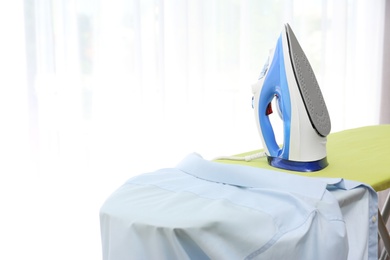 Photo of Board with modern iron and shirt at home. Laundry day