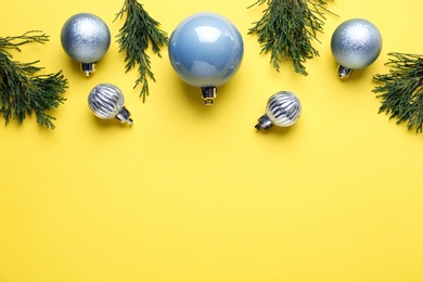 Photo of Beautiful blue Christmas balls and fir branches on yellow background, flat lay. Space for text