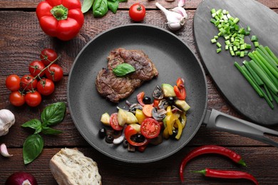 Photo of Tasty fried steak with vegetables in pan and ingredients on wooden table, flat lay